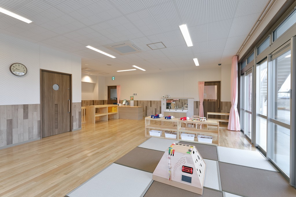 置き畳のプレイスペースと木製玩具棚を設けた、自然光が優しく差し込む明るい0歳児保育室